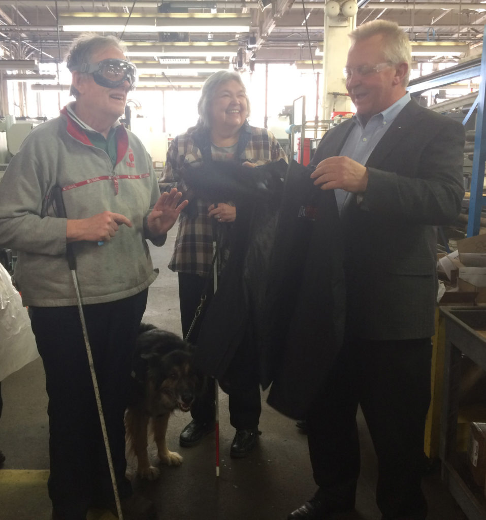 On the left, Gale stands laughing with Jackie in the center and her guide dog Valley and Jim Kerlin is on the right talking, smiling and holding a jacket.