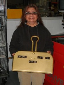 Sophia is smiling and holding a golden colored dust pan.