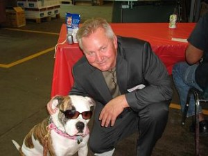 Jim Kerlin poses next to a brown and white dog wearing sunglasses.