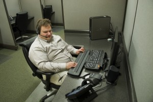 Steve sits at a comfortable desk with a computer and braille display on it.