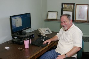 Gene Hubbard sits at a computer desk, smiling.