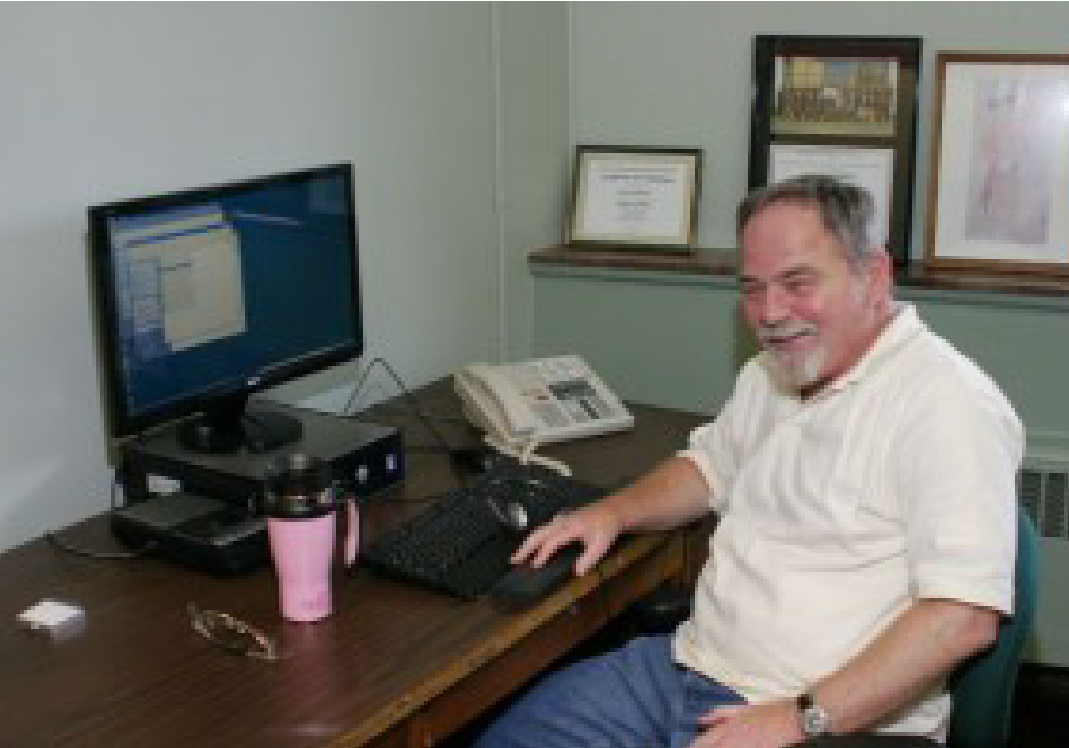 Gene Hubbard sits at a computer desk, smiling.