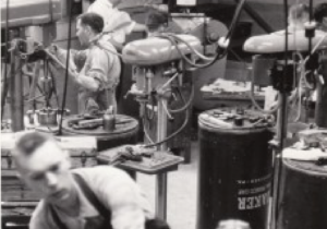 A black and white photo of a man who is blind working in a machine shop.