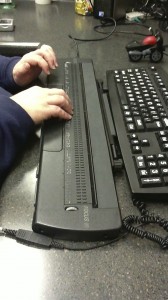 a pair of hand reading a braille display next to a keyboard for a computer.