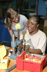 Frenchie talks with a co-worker as she is at an assembly work station.