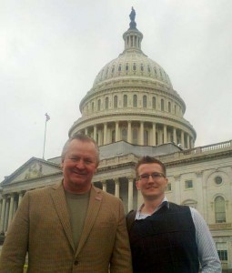 Two men stand smiling in front of the capitol building