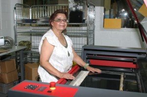 A woman wearing glasses is standing in front of a machine. She is placing a sheet of film into it. There are some buttons and knobs on the right side of the machine.