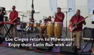 Los Ciegos return to Milwaukee! Enjoy their Latin flair with us! A band of musicians who are blind are playing. There are bongos, a drum set, keyboards and a bass player. All of them are wearing bright red shirts and khaki pants.