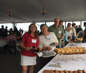 Sales Rep Linda Hapka standing with some guests at a table with a buffet of sandwiches.