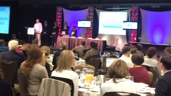 Stage with people holding awards and a man at a podium. Jim Kerlin is standing with an award on the stage, too.