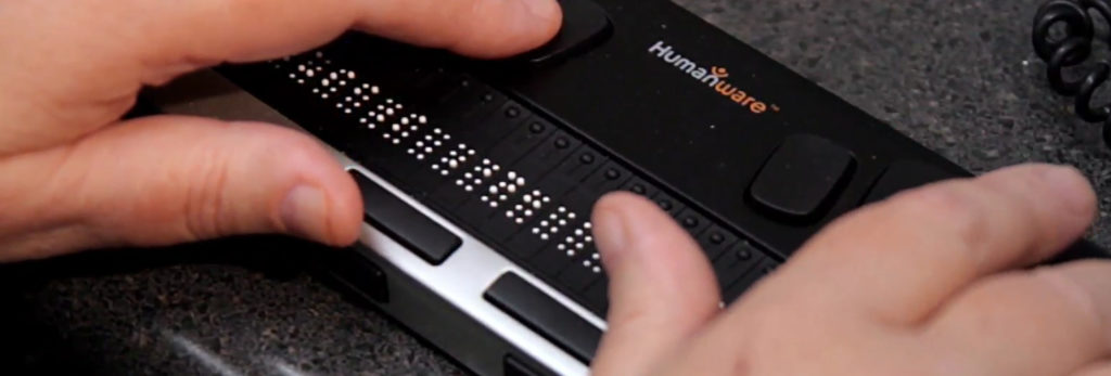 A pair of hands resting over a braille reader branded humanware.