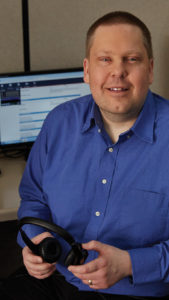 Jim Tess, Customer Care Specialist, sits in front of a computer smiling out at the camera.