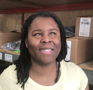 Renee Jones smiles happily at the camera. She is wearing a pale yellow top and has her hair in braids.