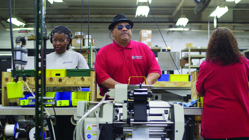 Julius and Renee are working at a machine that takes the parts they assembly and bags them.