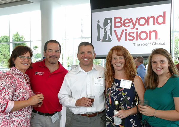 A group of people smiling as they stand in front of the Beyond Vision logo
