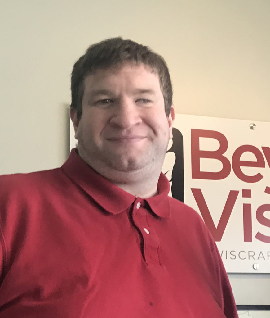 Ruben Rodriguez smiles as he stands in front of the Beyond Vision sign.