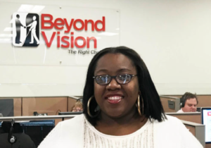 Picture of Beyond Vision employee Delonna standing in front of a Beyond Vision sign in our call center.