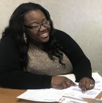 DeLonna sits at a table with paperwork smiling.