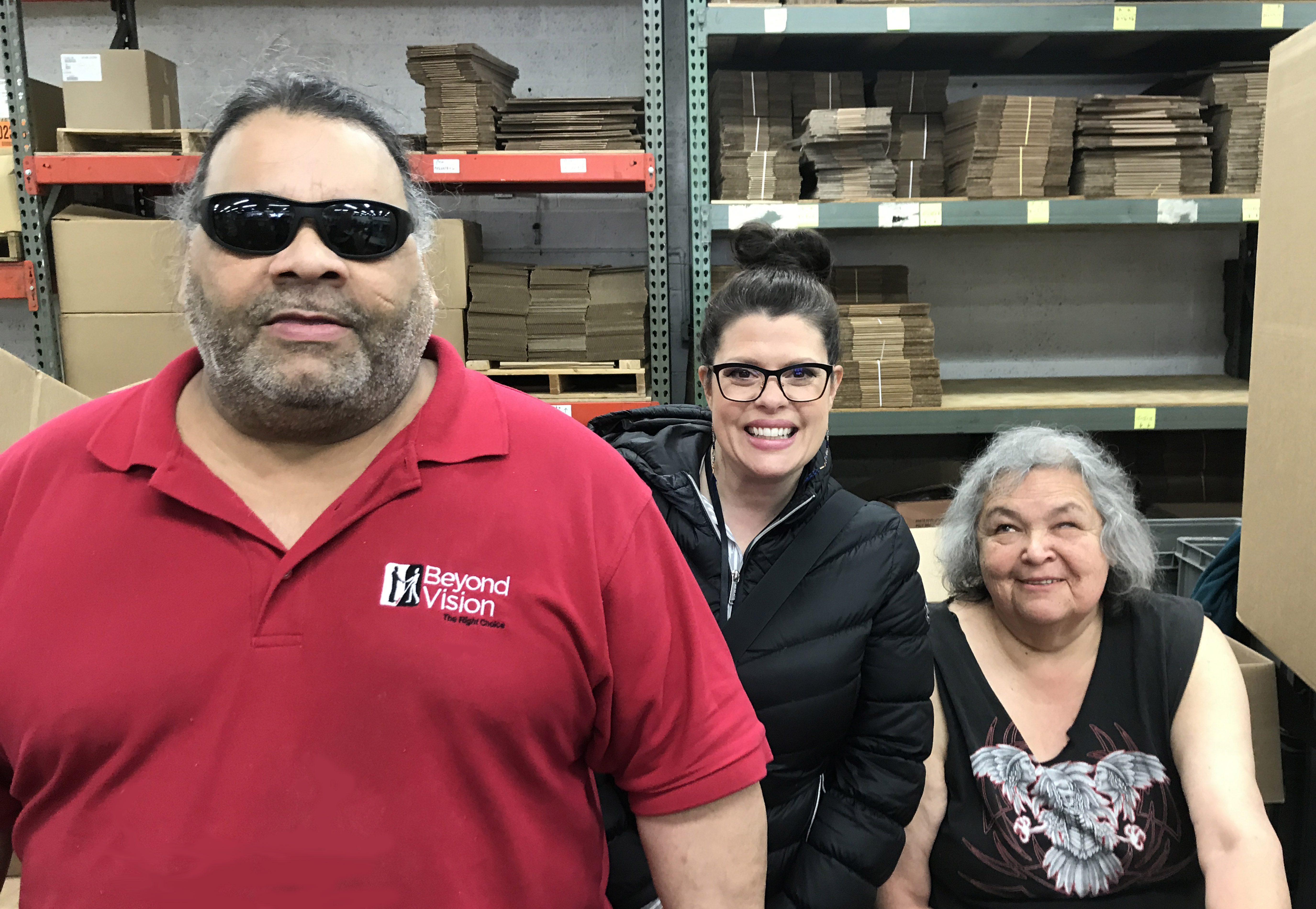 Julius stands wearing a red Beyond Vision shirt, Melissa and Jackie are smiling.