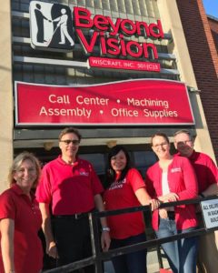 a group of five people stand in front of the Beyond Vision entrance. They are all wearing red shirts.