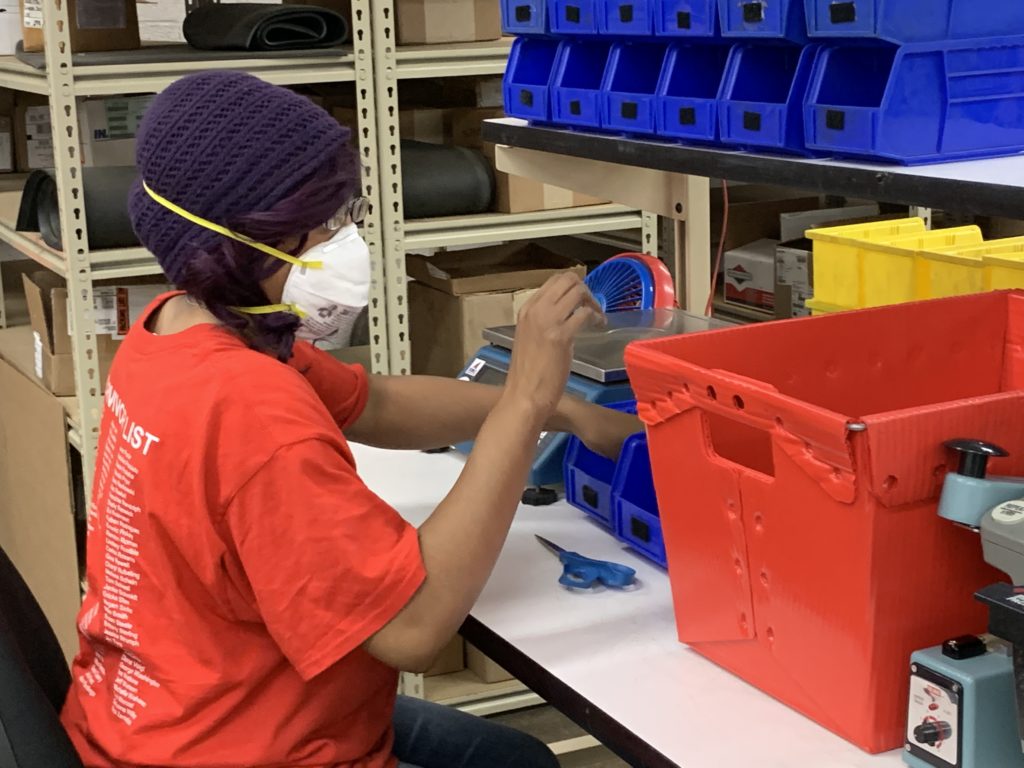 A person with vision loss is wearing an N95 mask and working at an assembly station.
