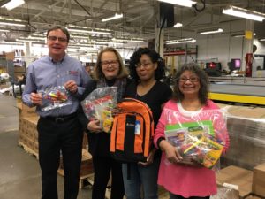 four people stand in a production area holding school supplies and backpacks