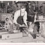 Black & White photo of a man in an apron holding a piece of metal