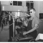 black and white image of a man with dark glasses operating a press.