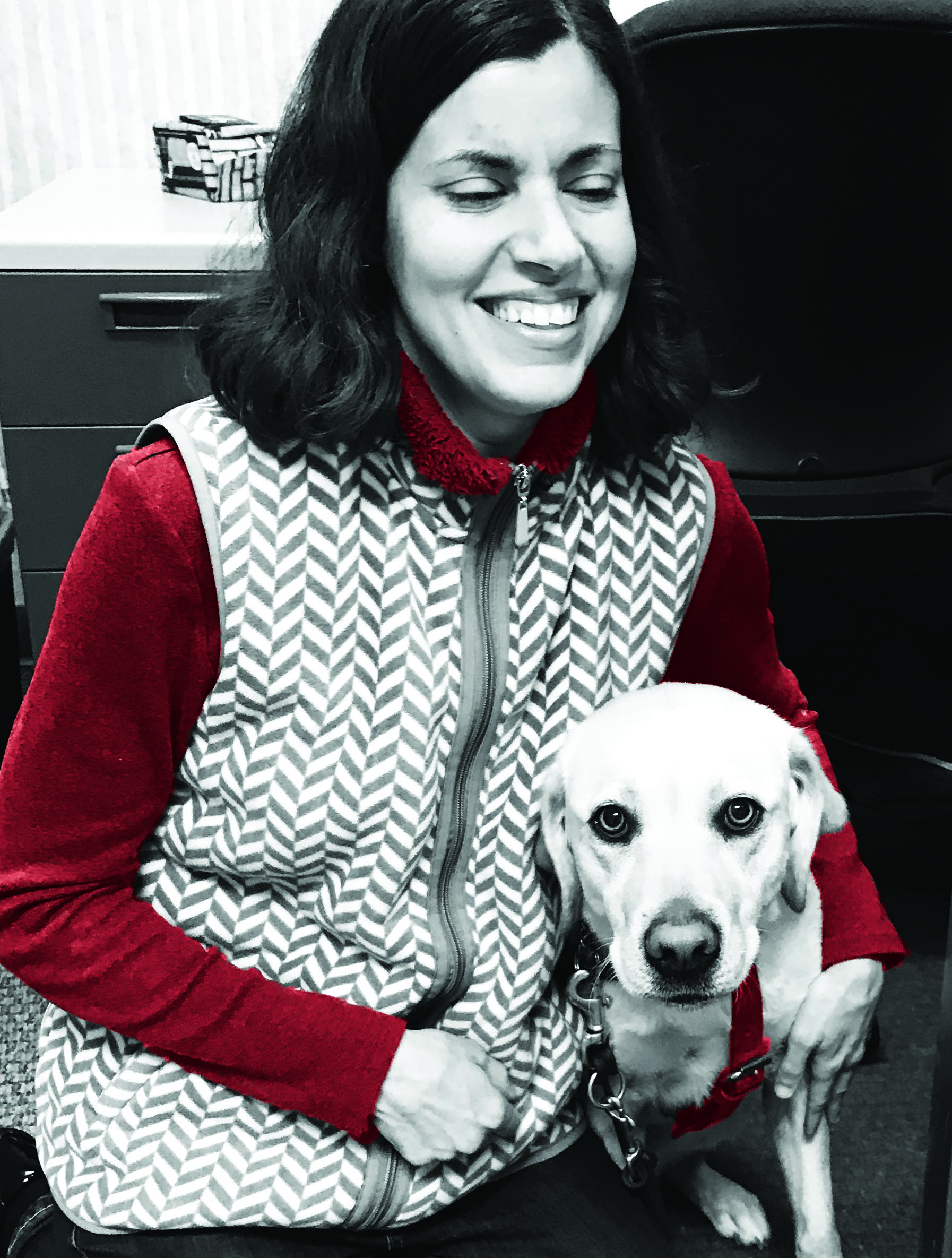 Stacy is smiling as she kneels next to guide dog Onida who is working. 