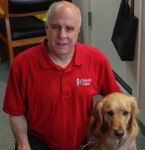 Scott wearing his Beyond Vision shirt and sitting next to his guide dog Lumi.