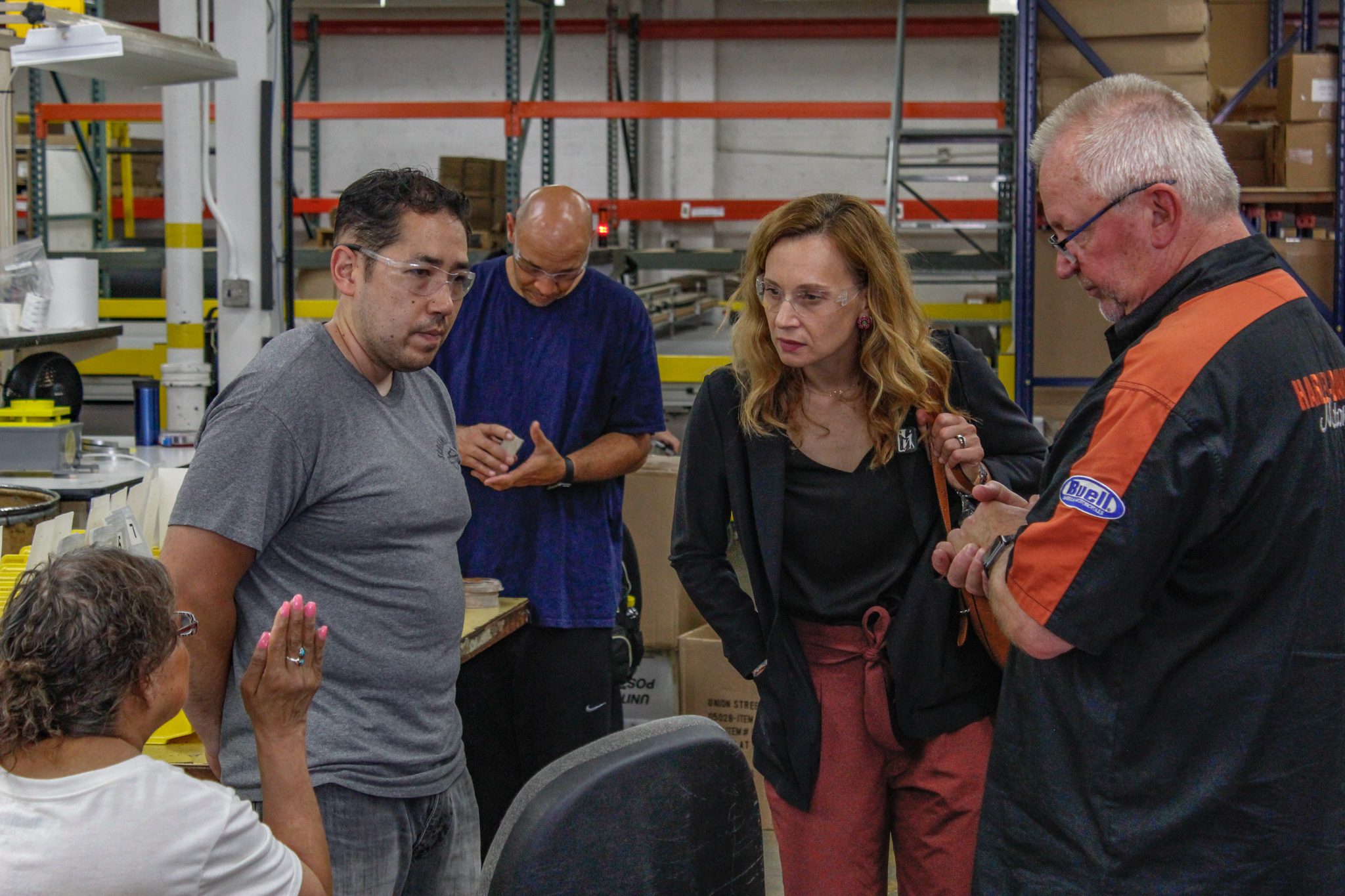 People are standing in an industrial space wearing safety glasses and talking.