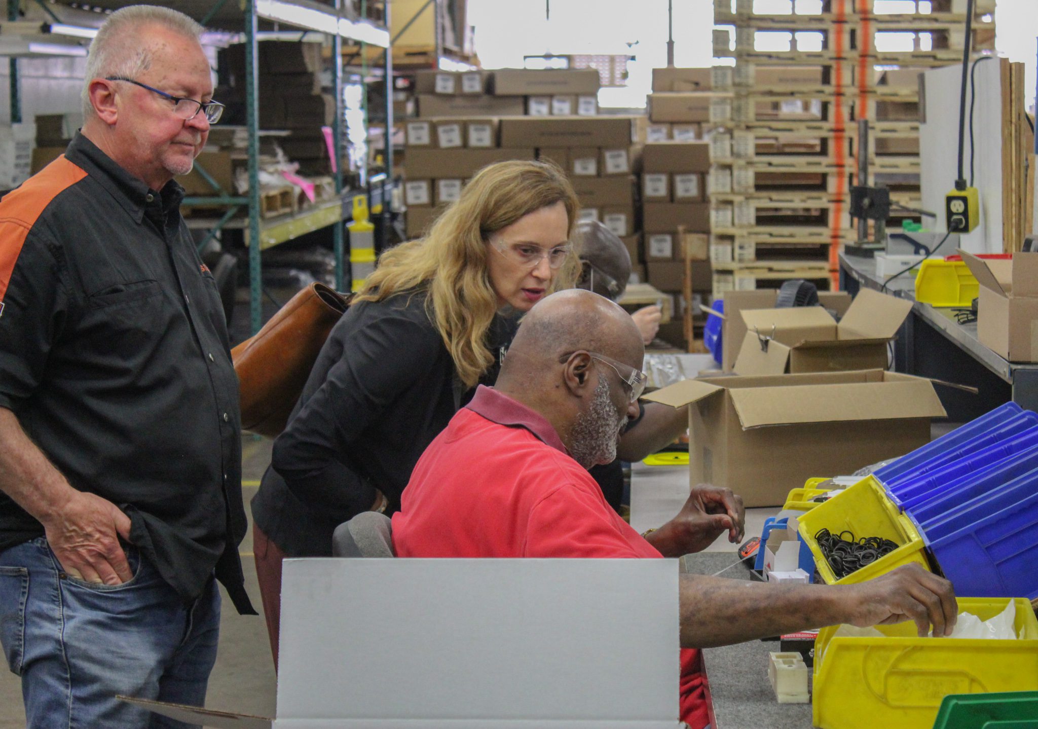 A man who is blind is showing a sighted woman what he is making on his workbench.