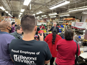 In the foreground, the back of a young man's t-shirts reads, Proud employee of Beyond Vision. Several others people are standing in the crowd and at the center is Senator Ron Johnson.