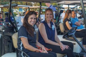 2 ladies sitting and smiling in their golf cart.
