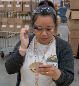 Photo of PangNhia Xiong using envision glasses to read a citytin coaster in the Assembly & Packaging department at Beyond Vision