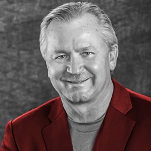 Black and white photo of Jim Kerlin smiling and wearing a bright red suit