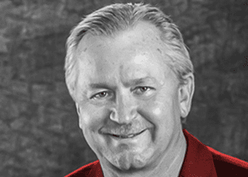 Black and white photo of Jim Kerlin smiling and wearing a bright red suit.