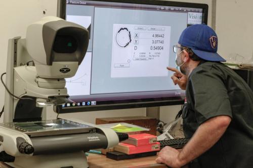 Beyond Vision employee, David measuring and inspecting a finished manufactured part on a zoomed screen.