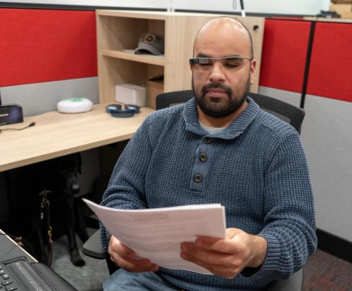 Photo of Israel wearing Envision glasses and holding a printed document.